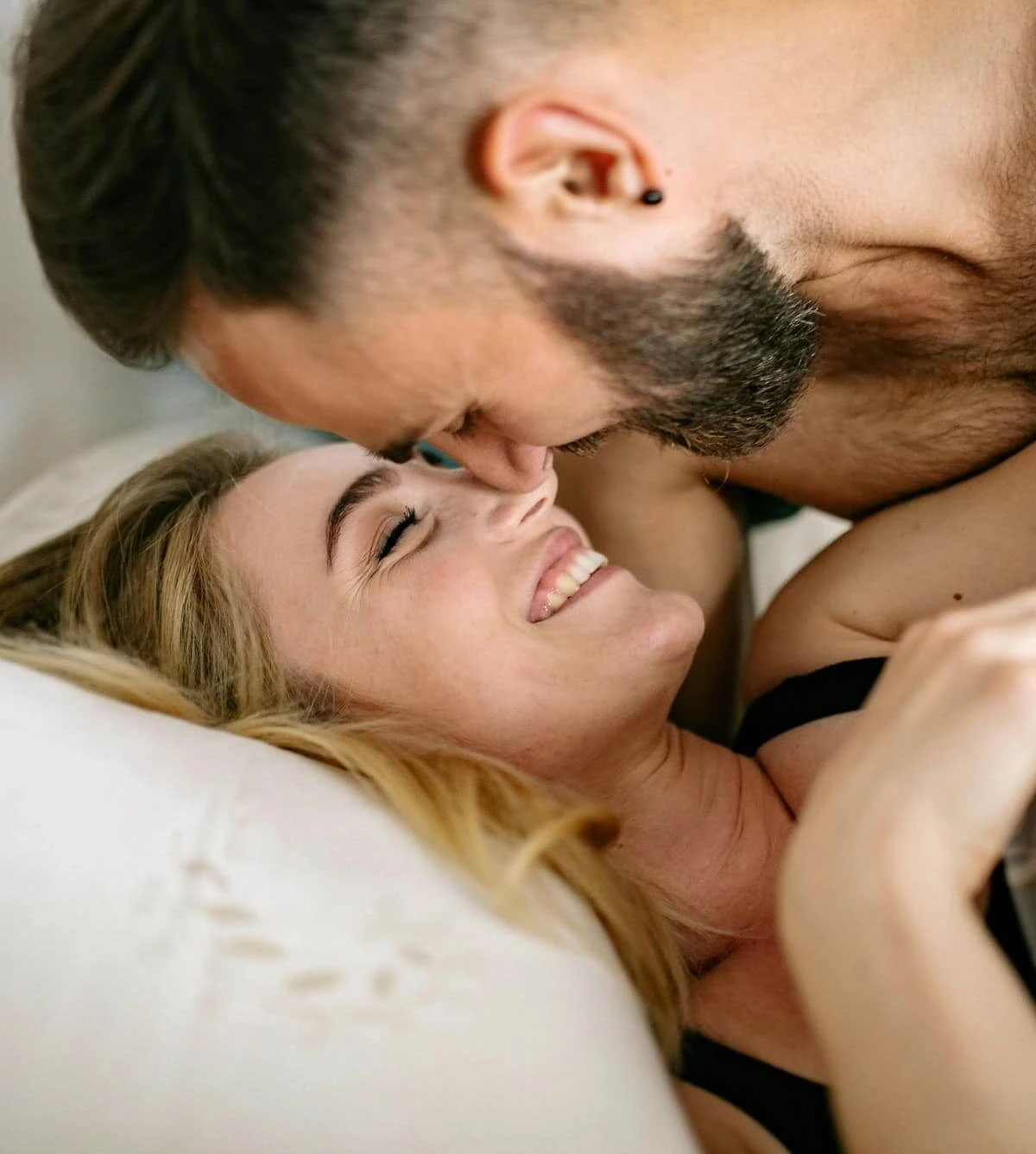 Pareja en la cama sonriendo mirándose a los ojos con la conexión del amor conciente y sexual